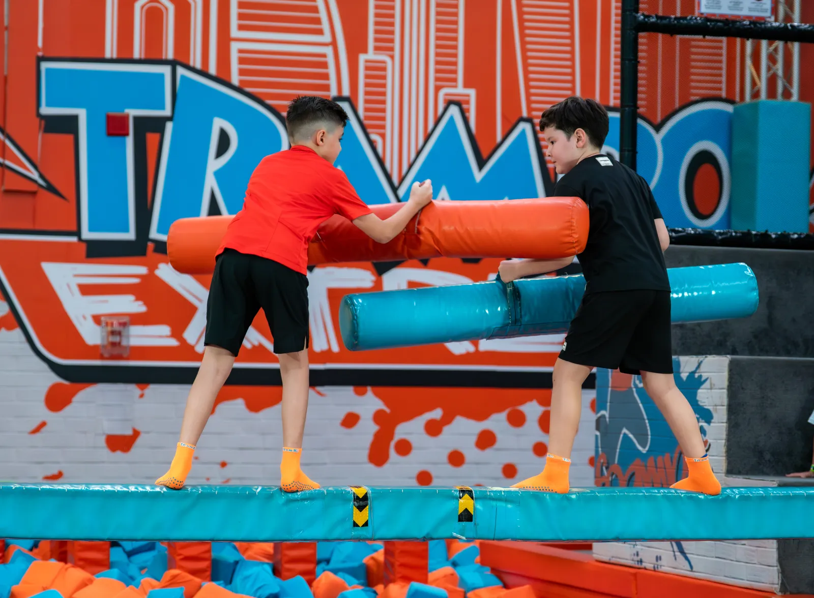 Boys competing head-to-head on the padded battle beam at Trampo UAE