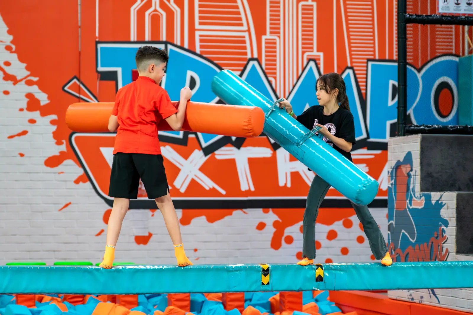 Players duelling with padded jousting sticks on the battle beam at Trampo