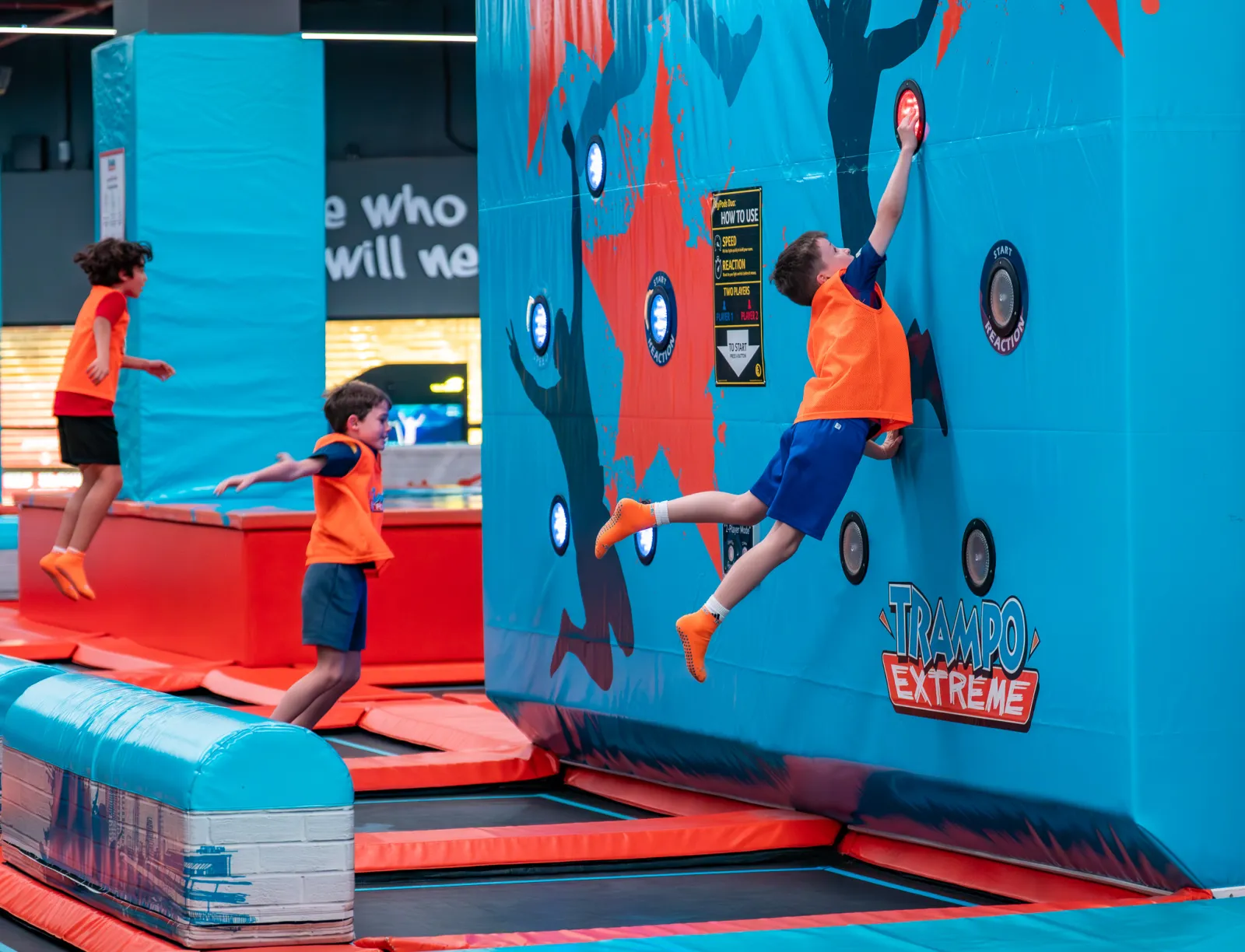 Kids mid-air hitting targets on the interactive wall at Trampo