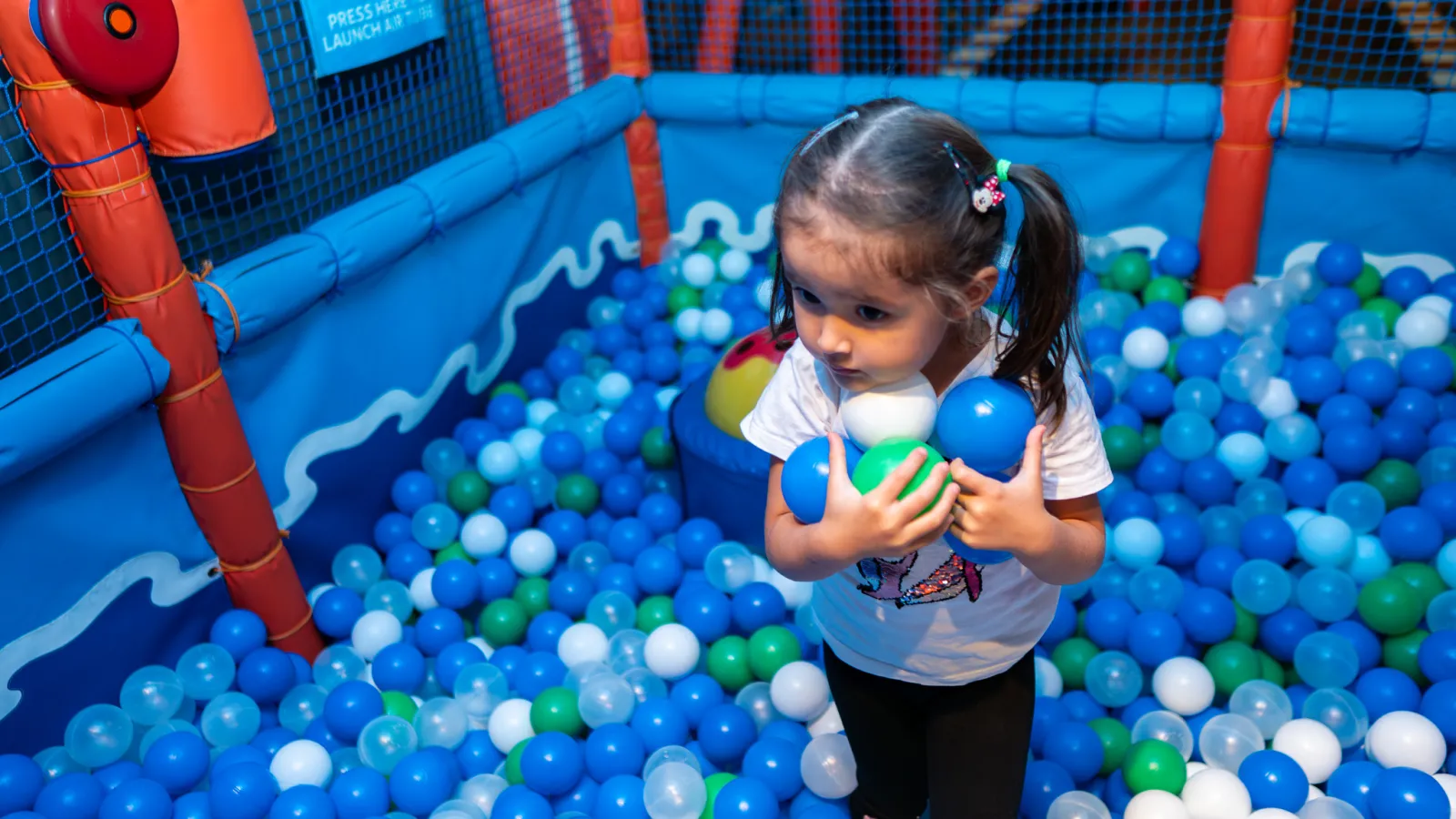 Girl holding colorful balls in the ball pit at Trampo