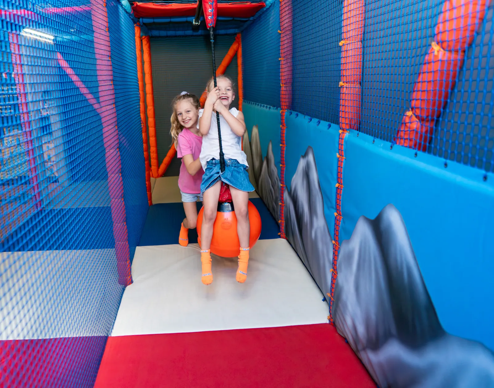 Two girls swinging on a rope swing in Trampo soft play